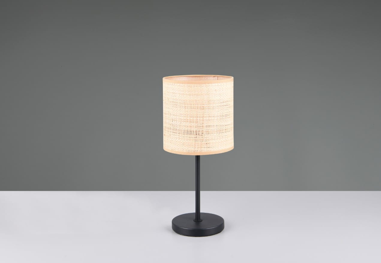 Lampa stołowa Aimee z czarną podstawą i naturalnym kloszem z wikliny. Stoi na płaskiej powierzchni, z okrągłą podstawą i cylindrycznym kloszem. Tło szare, co podkreśla minimalistyczny design lampy.