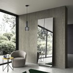 Lampa wisząca Amo w kolorze czarnym z oprawą E27, zawieszona na cienkim przewodzie. Kształt cylindryczny z perforowaną teksturą, umieszczona w nowoczesnym wnętrzu obok lustra, fotele i stół w tle.