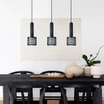 Lampa wisząca Amo 3xE27 w kolorze czarnym, z trzech cylindrycznych kloszy z siatkowym wzorem, zawieszona na długich linkach. Produkt umieszczony nad drewnianym stołem w nowoczesnej aranżacji, z białymi elementami dekoracyjnymi.