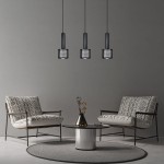 Lampa wisząca Amo 3xE27 w kolorze czarnym, z trzema cylindrycznymi kloszami o perforowanej strukturze, zawieszona na długich przewodach. W tle widoczne nowoczesne fotele i okrągły stół na szarym tle.