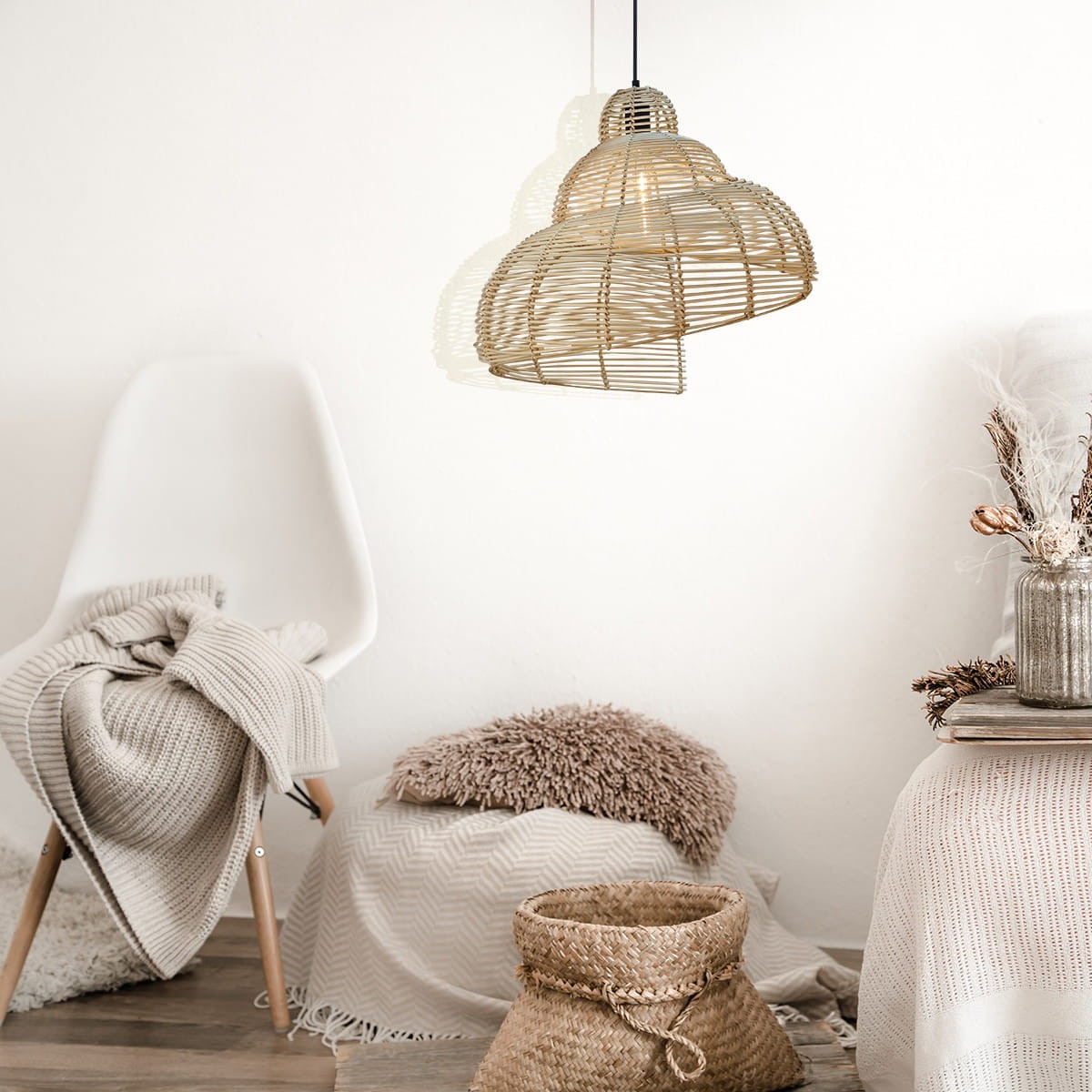 Lampa wisząca Shell D60 z czarnym metalowym elementem i rattanowym kloszem. Zawieszona na czarnym przewodzie, ma okrągły kształt. W tle widoczny fotel, pled i dekoracyjny kosz. Jasne tło podkreśla naturalne materiały.