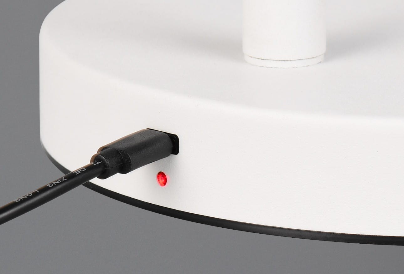 Biała lampa podłogowa Blake z portem USB, widok z boku. Na zdjęciu widoczny kabel podłączony do lampy oraz czerwony wskaźnik zasilania. Lampa ma okrągłą podstawę z czarną krawędzią.