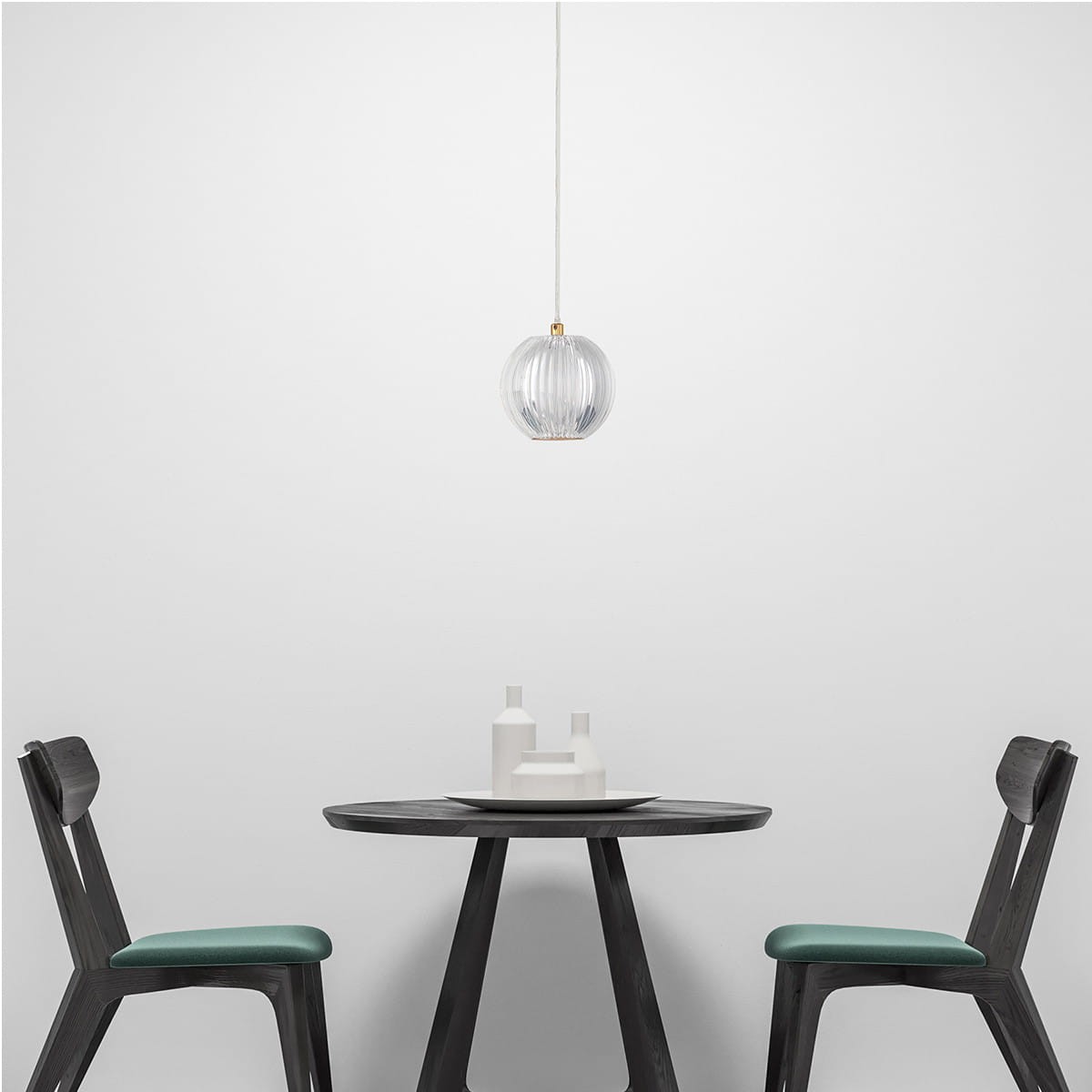 Lampa wisząca LED Brillant LP-3303/1P GD o okrągłym kształcie, wykonana ze szkła z delikatnymi żłobieniami, zawieszona na białym kablu. Złoty detal u góry. Widoczna w minimalistycznym wnętrzu z czarnym stołem i krzesłami.