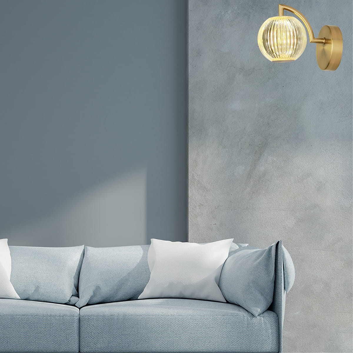 Kinkiet LED Brillant LP-3303/1W GD w złotym kolorze, z przezroczystym kloszem w kształcie kuli, zamontowany na ścianie obok niebieskiej kanapy. Oświetlenie w nowoczesnym stylu, emitujące ciepłe światło.