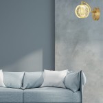 Kinkiet LED Brillant LP-3303/1W GD w złotym kolorze, z przezroczystym kloszem w kształcie kuli, zamontowany na ścianie obok niebieskiej kanapy. Oświetlenie w nowoczesnym stylu, emitujące ciepłe światło.
