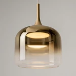 Lampa wisząca Spirito LED/12W w kolorze złotym, o szklanym kloszu z gradientem od przezroczystego do złotego. Ujęcie z dołu, pokazujące gładką, zaokrągloną formę oraz źródło światła wewnątrz klosza.