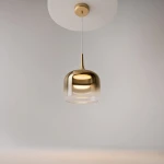 Lampa wisząca LED Spirito o mocy 12W w złotym kolorze, z półprzezroczystym kloszem o zaokrąglonym kształcie, zawieszona na cienkim przewodzie, z widoczną podstawą montażową w kolorze białym, na jednolitym tle.