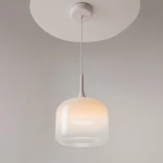 Biała lampa wisząca LED o mocy 12W z półprzezroczystym kloszem w kształcie cylindrycznym. Zawieszona na białym przewodzie, z okrągłym mocowaniem sufitowym. Emituje ciepłe światło, idealna do nowoczesnych wnętrz.