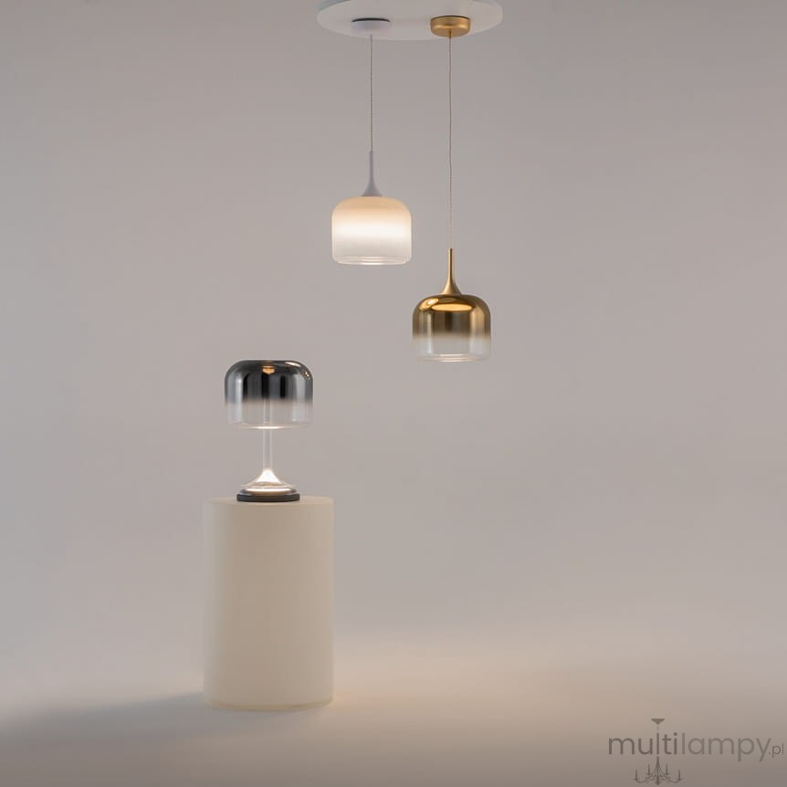 Lampa wisząca Spirito LED 12W w białej obudowie, z trzema różnymi kloszami: srebrnym, złotym i białym. Klosze mają różne kształty, w tym cylindryczny i stożkowy, zawieszone na długich linkach z sufitu. Produkt umieszczony na białym tle.