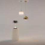 Lampa wisząca Spirito LED 12W w białej obudowie, z trzema różnymi kloszami: srebrnym, złotym i białym. Klosze mają różne kształty, w tym cylindryczny i stożkowy, zawieszone na długich linkach z sufitu. Produkt umieszczony na białym tle.