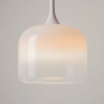 Lampa wisząca LED Spirito o mocy 12W, biała, z kloszem w kształcie kubka. Klosz ma gradientowy efekt kolorystyczny, przechodzący od bieli do delikatnego pomarańczu. Zawieszona na cienkim, białym przewodzie, w prostym otoczeniu.