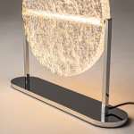 Lampa stołowa LED Mangata o mocy 7W w chromowanej podstawie. Wyposażona w okrągły klosz z fakturowanego szkła, emitująca ciepłe światło. Ujęta z boku, stojąca na prostokątnej podstawie, z widocznym przewodem elektrycznym.