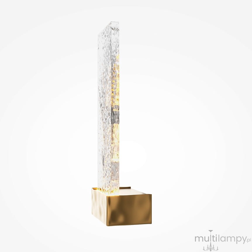 Lampa kinkiet LED o mocy 2W, wykonana z mosiądzu. Prosta, prostokątna forma z przezroczystym, teksturowanym kloszem, zamontowana na kwadratowej, złotej podstawie. Kinkiet prezentowany w pozycji stojącej, na jasnym tle.