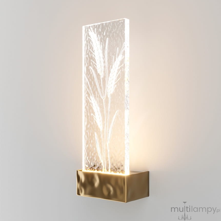 Kinkiet LED/2W w kolorze mosiądzu z przezroczystą, szklaną osłoną z wyraźnym wzorem roślinnym. Produkt zamontowany na ścianie, emitujący delikatne światło, z prostokątną formą i teksturą szkła.