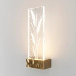 Kinkiet LED/2W w kolorze mosiądzu z przezroczystą, szklaną osłoną z wyraźnym wzorem roślinnym. Produkt zamontowany na ścianie, emitujący delikatne światło, z prostokątną formą i teksturą szkła.