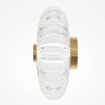 Kinkiet LED Amulet o mocy 8W, w złotej oprawie, z przezroczystym, teksturowanym kloszem, o okrągłym kształcie. Produkt zamontowany na ścianie, prezentujący nowoczesny design. Tło jasne, jednolite.