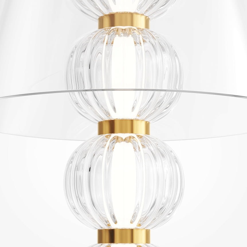 Lampa stołowa LED Amulet 10W w złotym kolorze, z przezroczystymi, falistymi elementami szklanymi, umieszczona na przezroczystym szkle. Widok z góry, ukazujący detale i strukturę lampy.