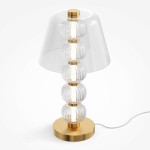 Lampa stołowa LED 10W w kolorze złotym z przezroczystym kloszem. Posiada sześć szklanych kul, które tworzą efektowną konstrukcję. Ustawiona na okrągłej podstawie, z przewodem elektrycznym widocznym z boku.