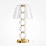 Lampa stołowa LED Amulet o mocy 10W, w złotym kolorze, z przezroczystym kloszem. Konstrukcja składa się z trzech przezroczystych kul, umieszczonych na okrągłej, złotej podstawie. Kabel zasilający widoczny z boku.