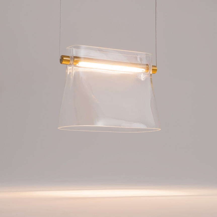 Lampa wisząca LED Cabaret o mocy 8W, wykonana z przezroczystego materiału z mosiężnym detalem. Ujęcie z przodu, lampa wisi na cienkim przewodzie. Oświetlenie umieszczone w górnej części klosza, nadające nowoczesny wygląd.