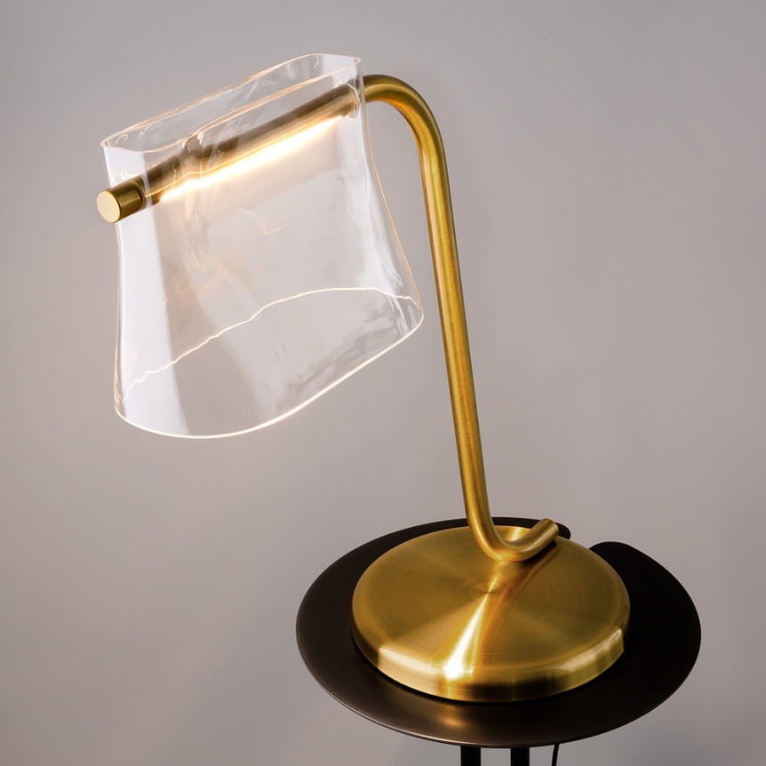 Lampa stołowa LED Cabaret o mocy 8W, wykonana z mosiądzu, z przezroczystym kloszem o falistym kształcie. Uchwyt w formie łuku, podstawa okrągła, kolor mosiężny. Ujęcie z boku, na jednolitym tle.