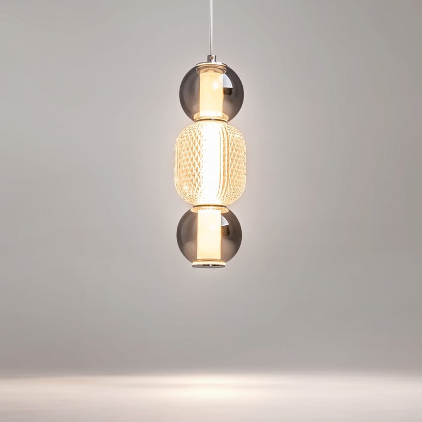 Lampa wisząca Drop 1xLED/16W w kolorze chromu, składająca się z trzech elementów: dwóch szklanych kul w odcieniach czerni i złotej, oraz środkowego, teksturowanego, przezroczystego klosza. Zawieszona na białym przewodzie w minimalistycznym otoczeniu.