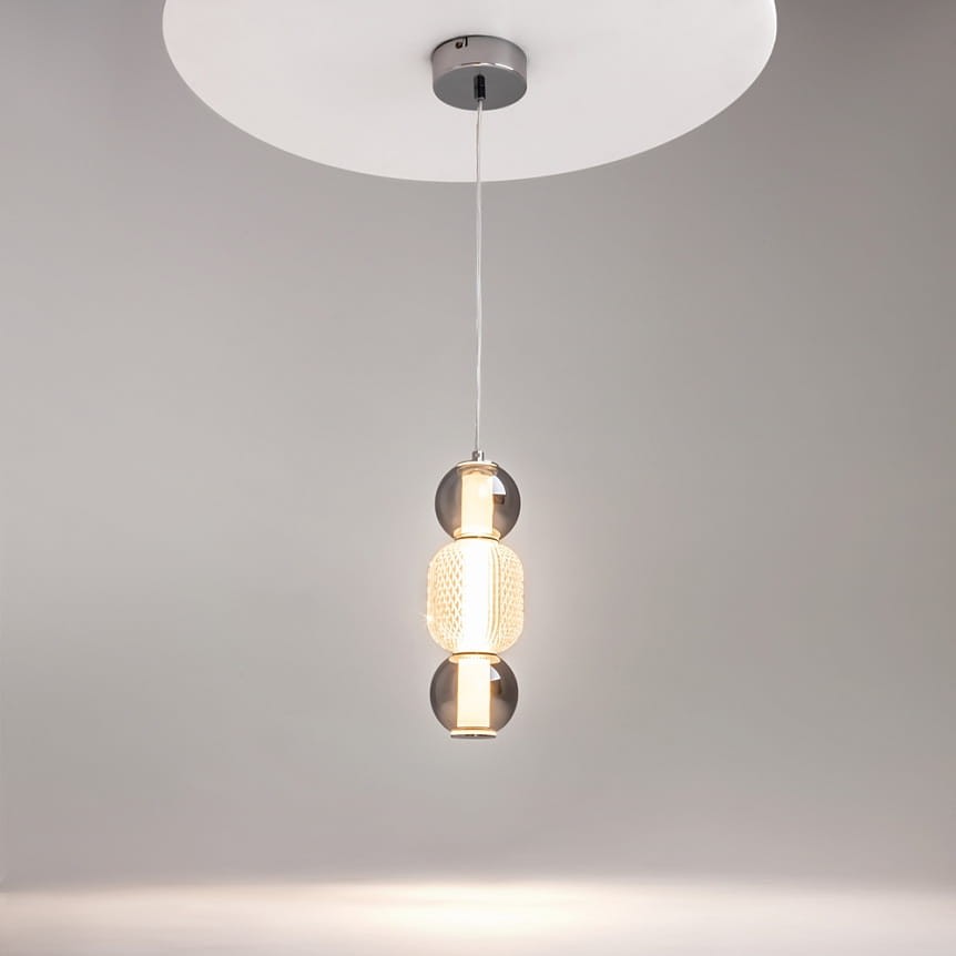 Lampa wisząca Drop 1xLED/16W w kolorze chromu, z przezroczystymi i siatkowanymi detalami. Ujęcie z góry, lampa zawieszona na cienkim przewodzie, emitująca ciepłe światło, na jednolitym szarym tle.