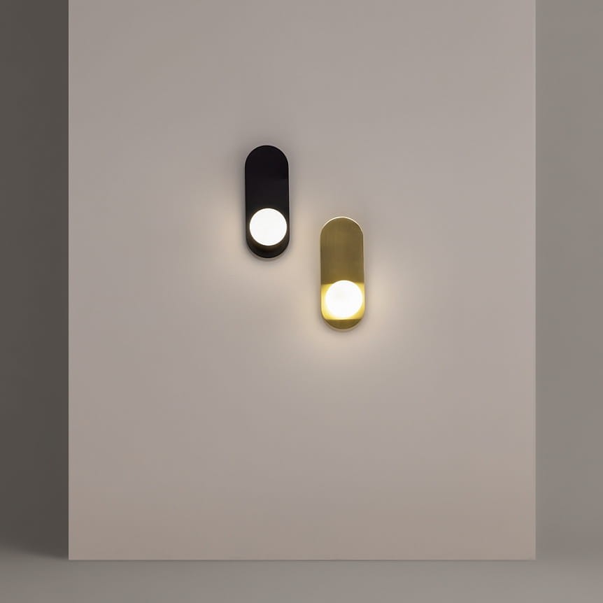 Kinkiet Bao 1xG9 w kolorze czarnym, o prostokątnym kształcie, zamontowany na jasnej ścianie. W górnej części znajduje się okrągła żarówka, emitująca światło. Obok widoczny kinkiet w kolorze złotym, co tworzy kontrast.