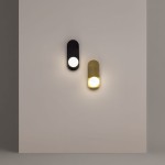 Kinkiet Bao 1xG9 w kolorze czarnym, o prostokątnym kształcie, zamontowany na jasnej ścianie. W górnej części znajduje się okrągła żarówka, emitująca światło. Obok widoczny kinkiet w kolorze złotym, co tworzy kontrast.