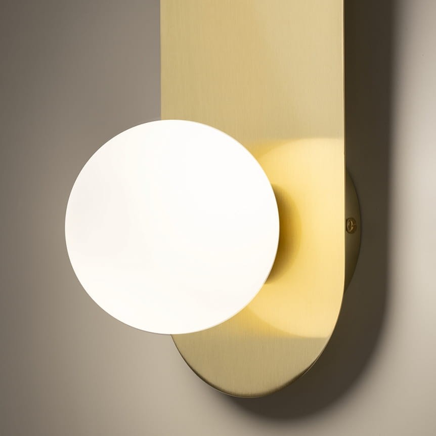 Kinkiet Bao w kolorze złotym z okrągłym, białym kloszem. Ujęcie z boku, pokazujące gładką, metalową podstawę oraz delikatne światło emitowane przez klosz. Idealny do nowoczesnych wnętrz.