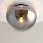 Czarna lampa sufitowa Glassy z dymioną szklaną kopułą i żarówką E27, zamontowana na suficie. Widoczny detal metalowego mocowania oraz wydobywające się światło z żarówki. Proste tło podkreśla elegancki design lampy.
