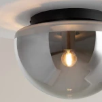 Czarna lampa sufitowa Glassy z dymionym kloszem, z oprawą na żarówkę E27. Widok z boku, ukazujący szklany klosz i żarówkę w środku, zamontowana na suficie. Klosz ma półprzezroczystą, zaokrągloną formę.