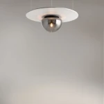 Lampa sufitowa Glassy z jedną oprawą E27 w kolorze czarnym i dymionym, z metalowym kloszem w kształcie kuli, zawieszona na cienkich linkach, z okrągłą, białą podstawą. Ujęcie z dołu, na tle szarej ściany.