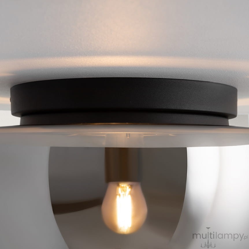 Czarna lampa sufitowa Glassy z dymionym kloszem, z widoczną żarówką E27. Ujęcie z bliska, pokazujące detal mocowania i kształt klosza, który odbija światło. Produkt zamontowany na gładkim, jasnym suficie.