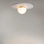 Lampa sufitowa Glassy 1xE27 w kolorze złotym i białym. Okrągła, matowa osłona z białego szkła zawieszona na płaskim, złotym mocowaniu. Produkt wisi na cienkich linkach, na jednolitym, szarym tle.