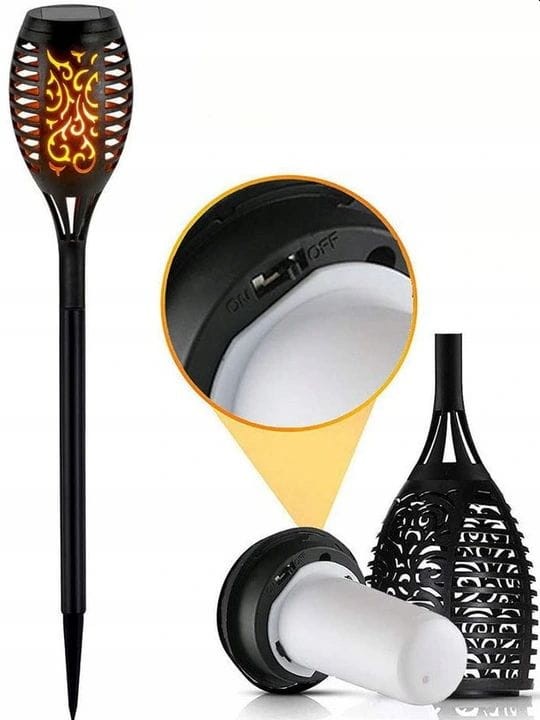 Czarna lampa solarna ogrodowa w formie pochodni, wbijana, z efektem LED. Widoczna koronkowa obudowa z dekoracyjnym wzorem. Zbliżenie na włącznik ON/OFF i źródło światła. Wysokość 50 cm, idealna do oświetlenia przestrzeni na zewnątrz.