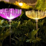 Dwie lampy solarne w kształcie dmuchawca, jedna w kolorze fioletowym, druga złota, na metalowych stelażach. Lampy świecą LED, umieszczone w zielonym otoczeniu roślin, dodają dekoracyjnego akcentu do ogrodu. Wysokość 74 cm.