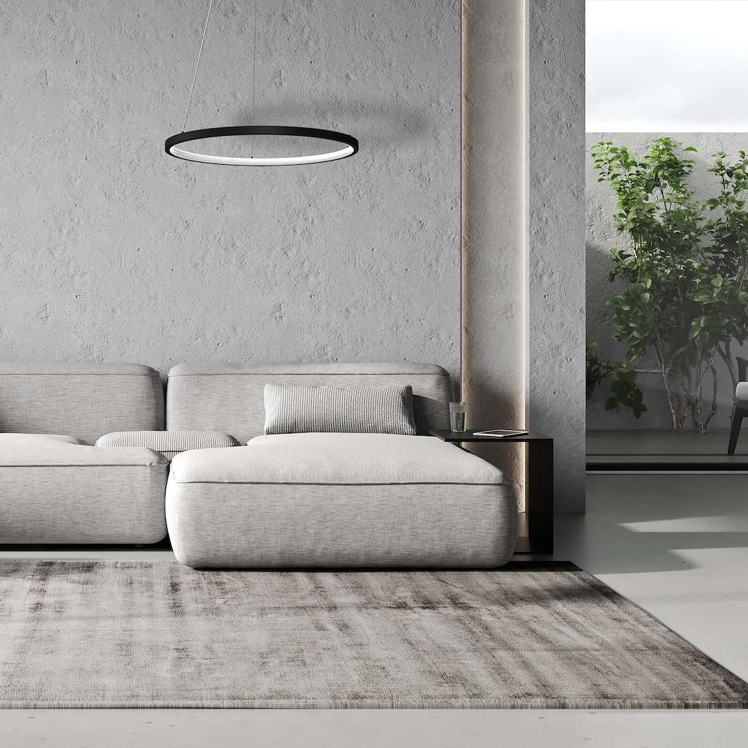 Lampa wisząca LED Hoop 27W w czarnym kolorze, o okrągłym kształcie, zawieszona na cienkich linkach. Widoczna w nowoczesnym wnętrzu z szaro-beżową kanapą i stolikiem. Tło neutralne, z roślinnością w tle.