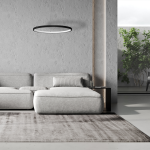 Lampa wisząca LED Hoop 27W w czarnym kolorze, o okrągłym kształcie, zawieszona na cienkich linkach. Widoczna w nowoczesnym wnętrzu z szaro-beżową kanapą i stolikiem. Tło neutralne, z roślinnością w tle.