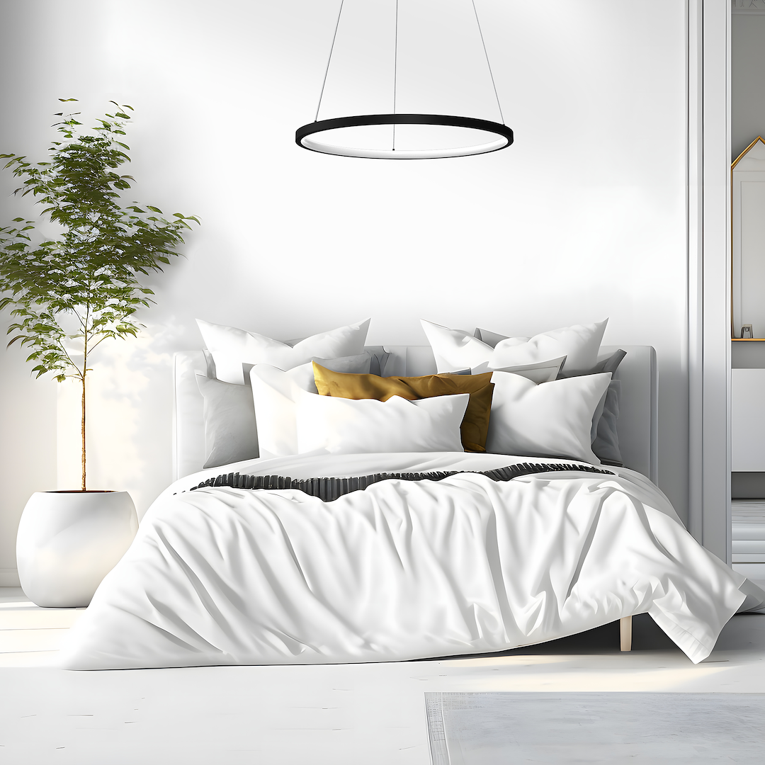 Czarna lampa wisząca LED o mocy 27W, okrągła, zawieszona nad białym łóżkiem z poduszkami w różnych odcieniach. Tło jasne, minimalistyczne, z zieloną rośliną w doniczce. Lampa podkreśla nowoczesny styl aranżacji wnętrza.
