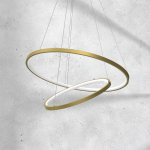 Lampa wisząca Hoop z dwoma okręgami, złota konstrukcja z białym podświetleniem LED, zawieszona na cienkich linkach. Okręgi mają różne średnice, co tworzy nowoczesny efekt. Tło w odcieniach szarości.