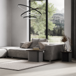 Lampa wisząca Hoop z trzema źródłami LED w kolorze czarnym, zawieszona nad szarym narożnikiem, z oknem w tle, przez które widać zieleń oraz góry. Kształt lampy to trzy okręgi, co nadaje nowoczesny wygląd.
