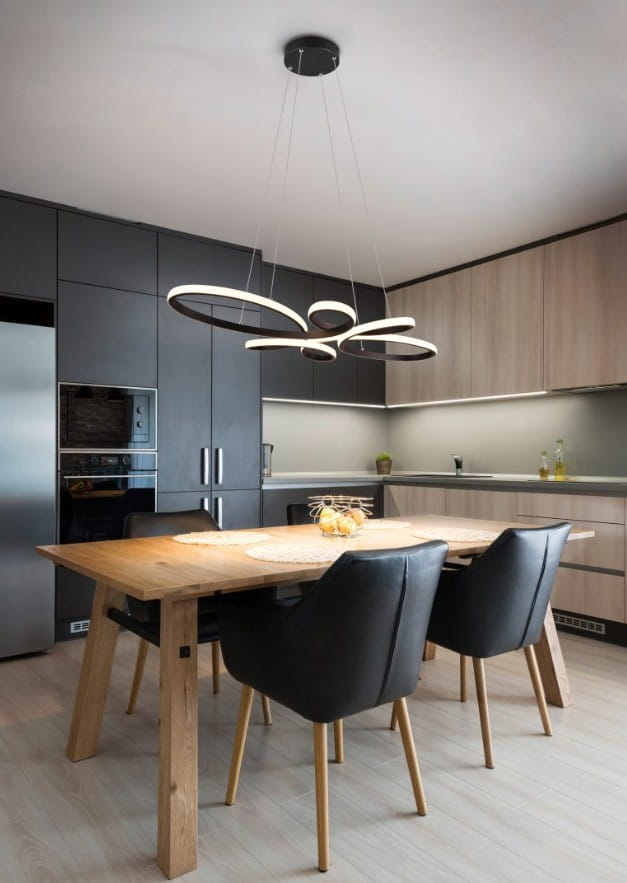 Lampa wisząca Fly w kolorze czarnym z jednym źródłem LED o mocy 32W i ciepłej barwie 3000K, zawieszona na cienkich linkach, umieszczona nad drewnianym stołem w nowoczesnej kuchni z szarymi i jasnymi meblami.