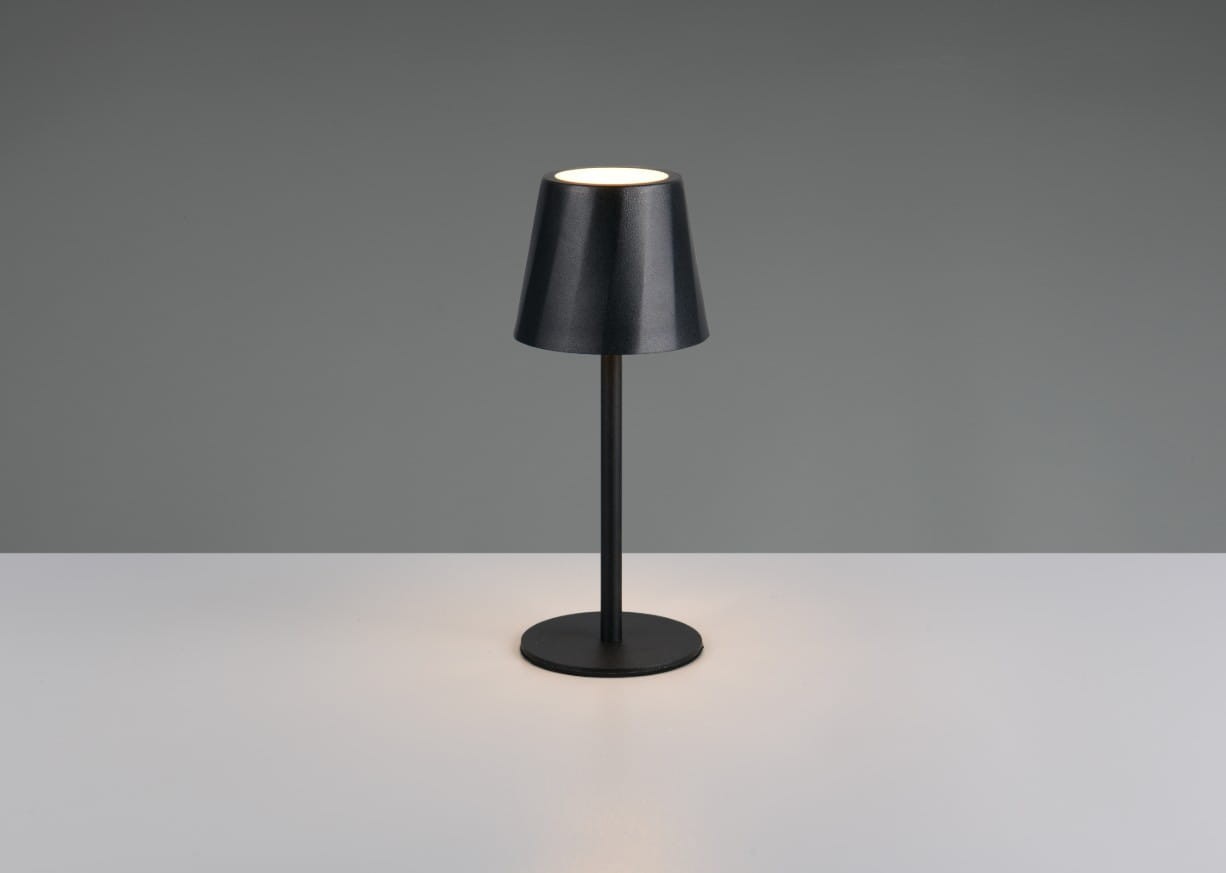 Czarna lampa stołowa zewnętrzna Diaz, z jedną diodą LED o mocy 1,6W, posiada cylindryczny klosz oraz okrągłą podstawę. Ujęcie frontalne na białym blacie, z subtelnym podświetleniem. Idealna do aranżacji przestrzeni na świeżym powietrzu.