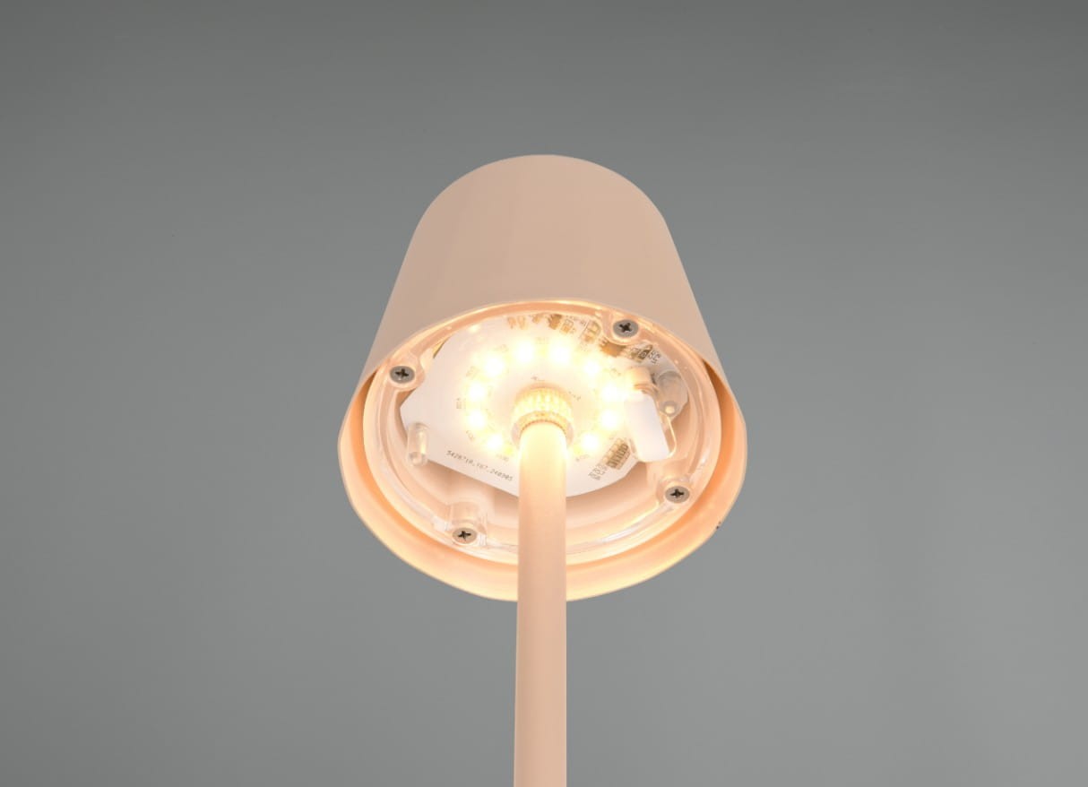 Lampa stołowa zewnętrzna Diaz w kolorze piaskowym, z montażem na stół. Zbliżenie na górną część lampy z widoczną diodą LED 1,6W oraz okrągłym kloszem. Elementy mocujące oraz źródło światła są dobrze widoczne. Tło szare.