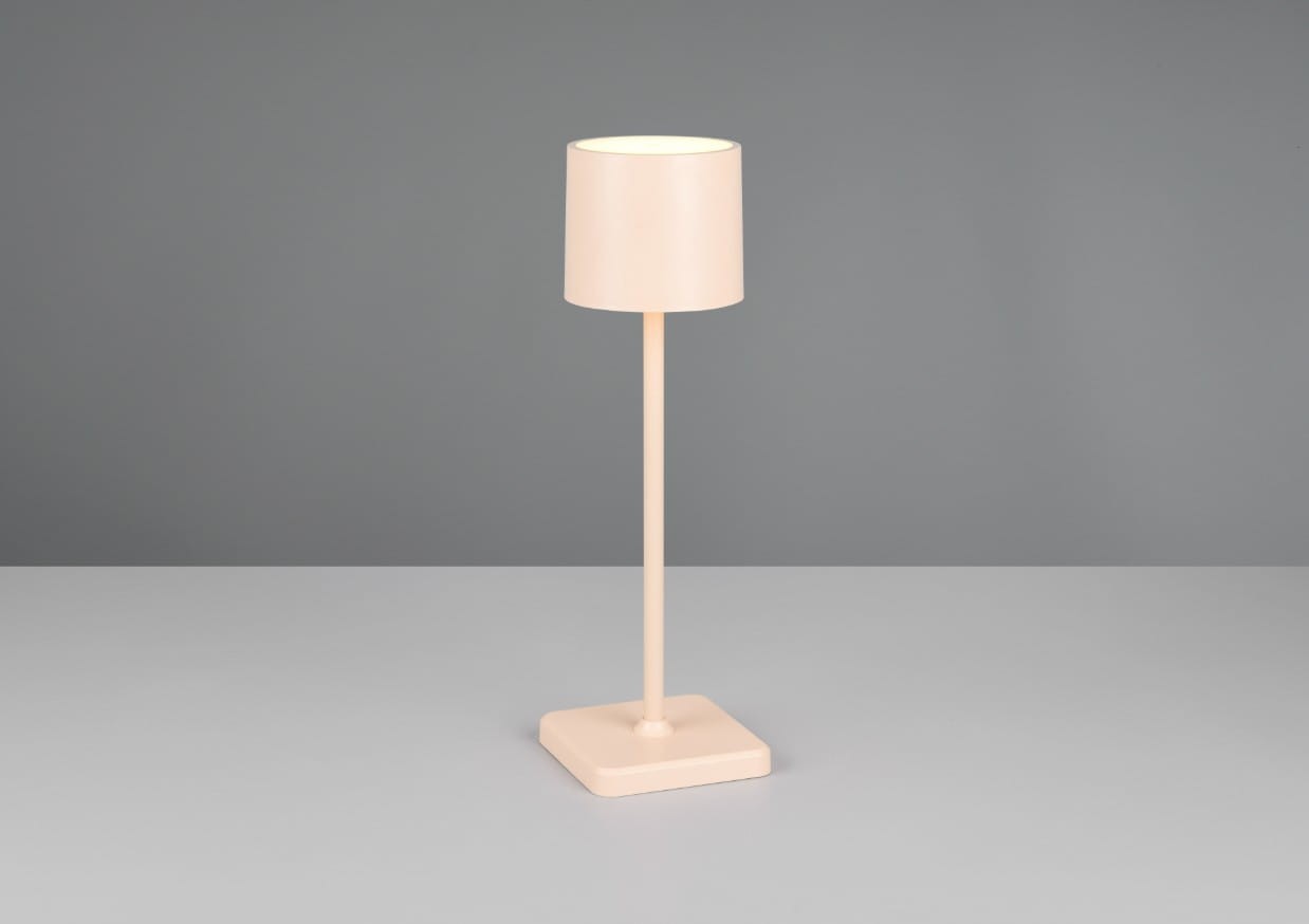 Lampa stołowa zewnętrzna Fernandez w kolorze piaskowym, z cylindrycznym kloszem i prostą, smukłą podstawą. Produkt stoi na płaskiej powierzchni, prezentując minimalistyczny design. W zestawie 1xLED 1,5W/CCT.