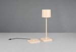 Lampa stołowa zewnętrzna Fernandez w kolorze piaskowym, z cylindrycznym kloszem i prostą podstawą. Ujęcie frontalne, lampa stoi na stole obok kwadratowej podstawy z przewodem USB. Wysokość lampy pozwala na oświetlenie małych przestrzeni.