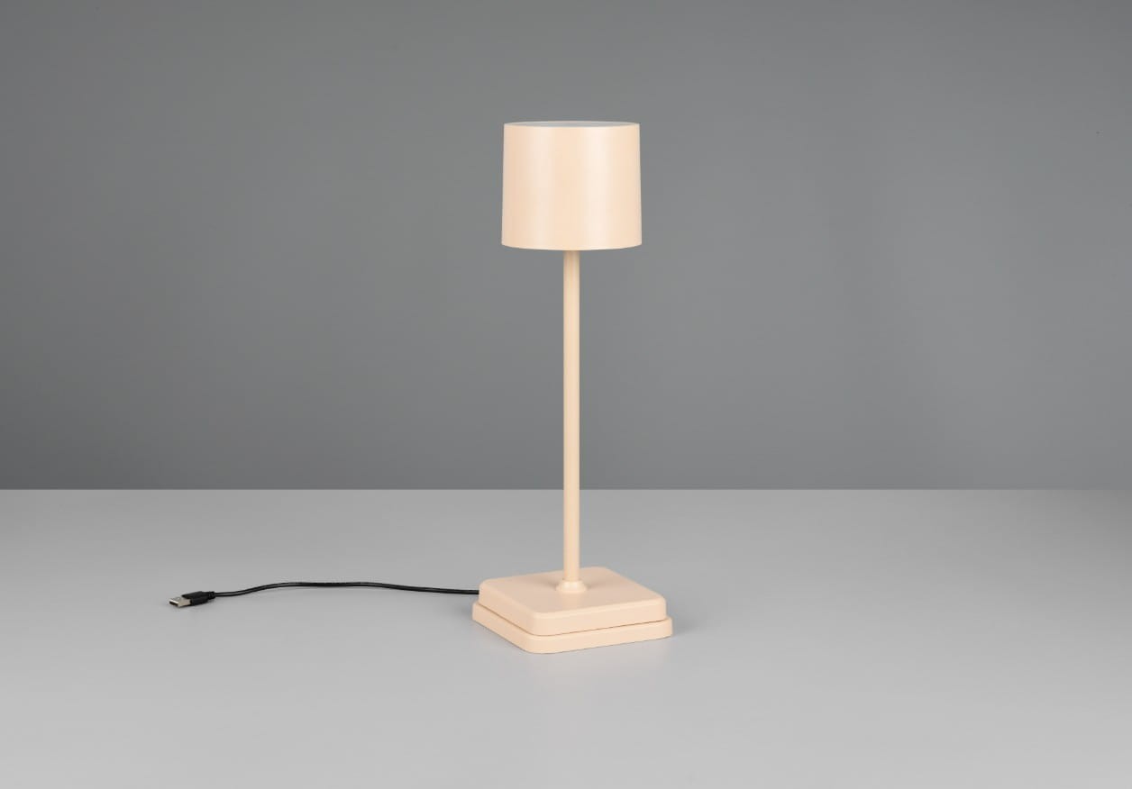 Lampa stołowa zewnętrzna Fernandez w kolorze piaskowym, z cylindrycznym kloszem na smukłym stelażu. Ustawiona na kwadratowej podstawie, z widocznym kablem zasilającym. Idealna do oświetlenia przestrzeni na świeżym powietrzu.