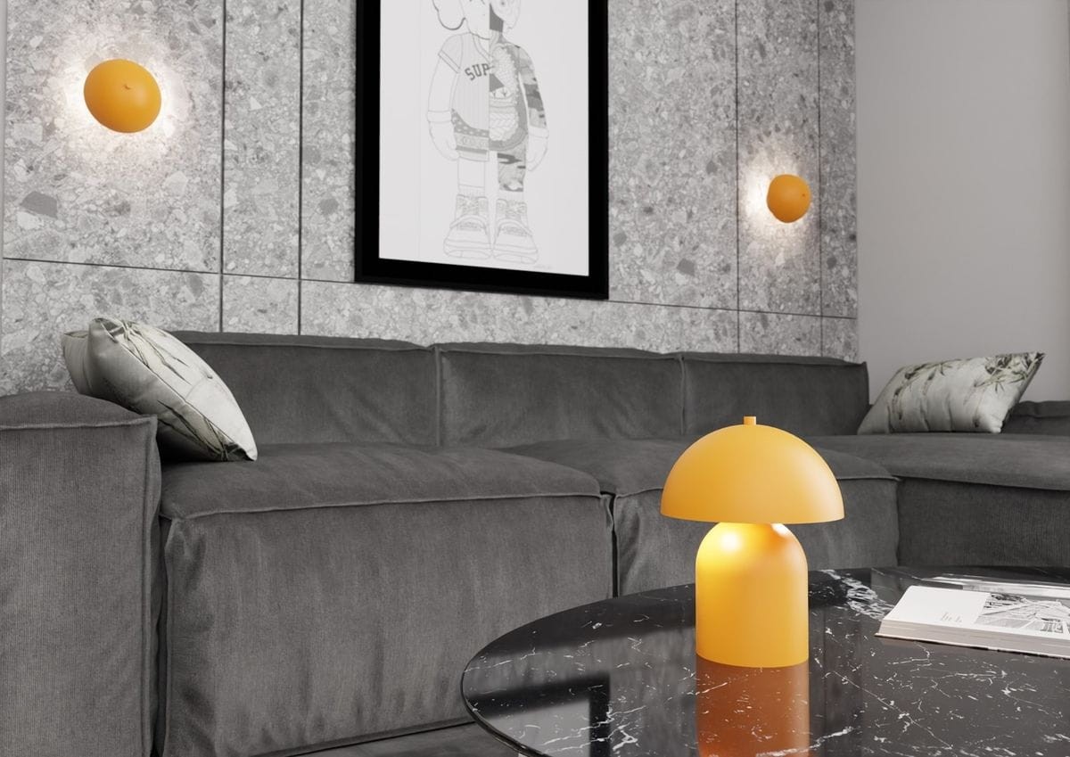 Lampa stołowa Mush w kolorze pomarańczowym z kloszem o kształcie półkuli, wykonana z matowego materiału. Ustawiona na czarnym, okrągłym stole kawowym, w tle szary narożnik i grafika na ścianie.