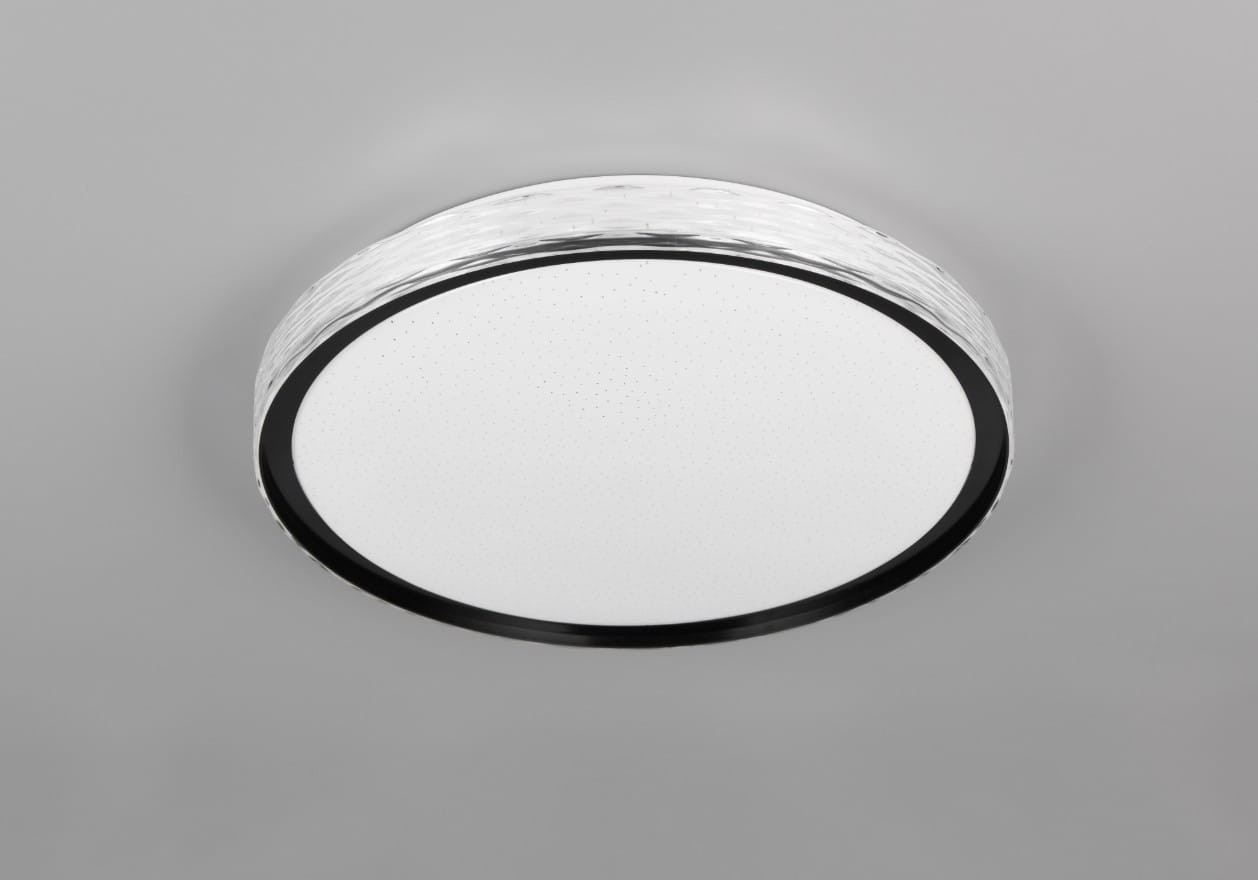 Plafon Varda w kolorze czarnym, okrągły, z białą, gładką powierzchnią i dekoracyjnym brzegiem. Wyposażony w pilot, 1x LED o mocy 24W, możliwość zmiany temperatury barwowej światła. Zawieszony na szarym tle, w pozycji montażowej.